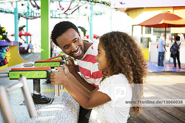 Vater schauendes Mädchen beim Spielen mit der Wasserpistole im Vergnügungspark