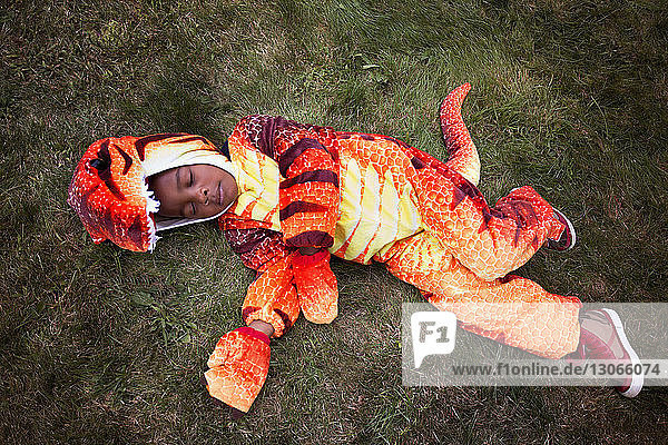 Hoher Engel Ansicht eines Jungen in Dinosaurier-Kostüm  der während Halloween im Hof schläft