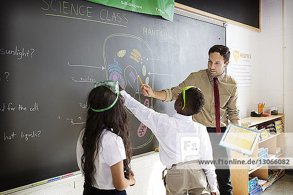 Teacher explaining to students while standing by blackboard in classroom