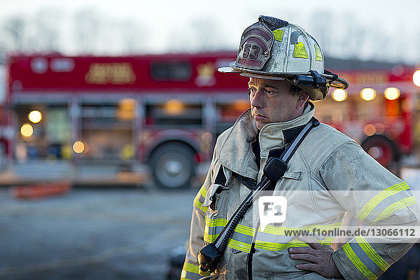 Tired firefighter looking away while standing against fire engine