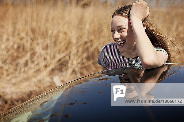 Happy woman looking away while leaning on car