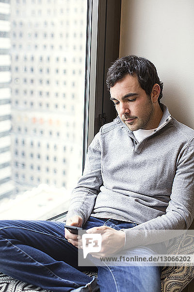 Man using smart phone while sitting on window seat at home