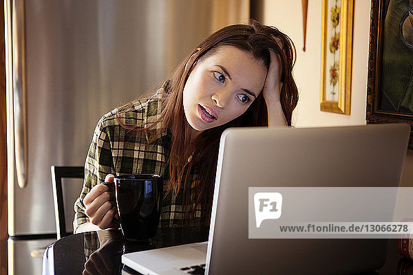 Kaffeetasse einer Frau  die zu Hause am Laptop sitzt