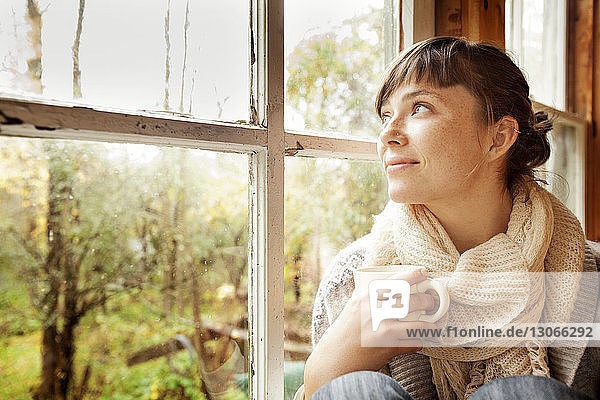 Frau schaut weg  während sie zu Hause am Fenster sitzt