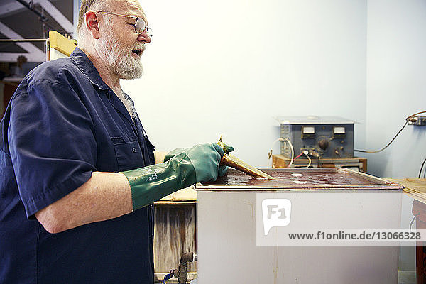 Seitenansicht des Mannes  der während der Arbeit in der Werkstatt die Trompete in Lösung taucht