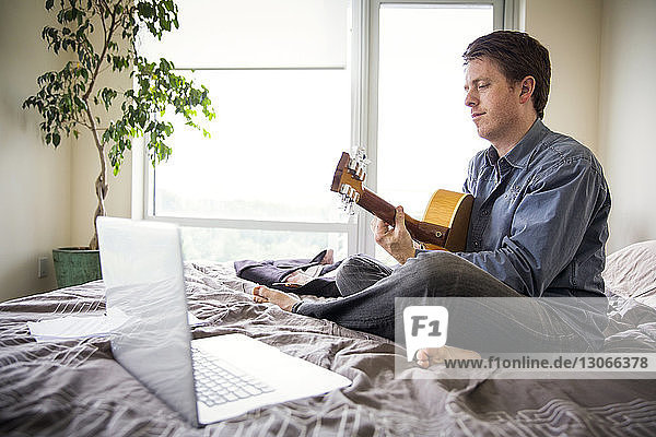 Mann benutzt Laptop-Computer  um zu Hause Gitarre zu lernen