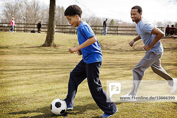Seitenansicht von Vater und Sohn beim Fussballspielen auf dem Spielfeld im Park