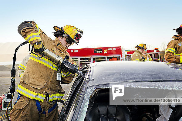 Feuerwehrmann schneidet Autofenster auf  während er gegen den klaren Himmel steht
