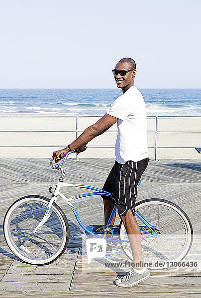 Man with bicycle standing on pier against beach