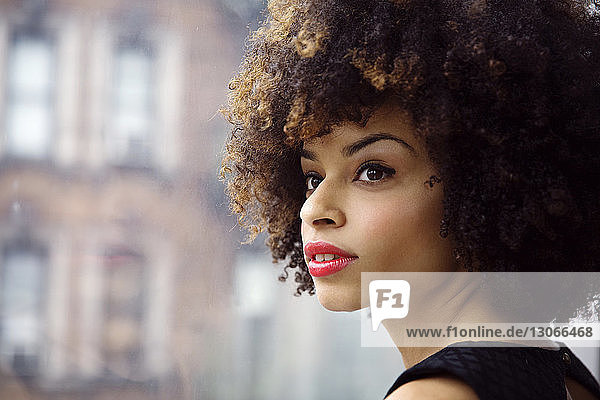 Close-up of thoughtful woman with curly hair looking away while standing by window