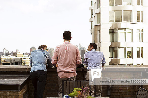 Rear view of friends talking while standing at retaining wall in building terrace