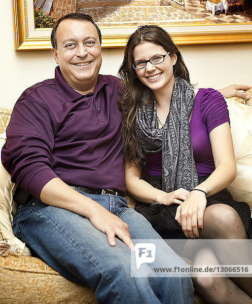 Portrait of father and daughter sitting on sofa at home