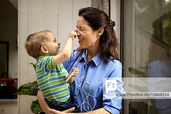 Verspielter Sohn kneift der Mutter in die Nase  während er zu Hause das Handy hält