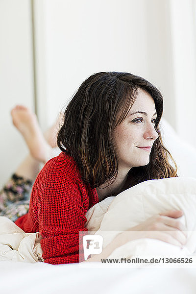 Lächelnde Frau schaut weg  während sie zu Hause auf dem Bett liegt