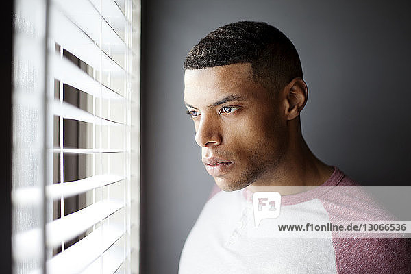 Man looking away while standing by blinds at home