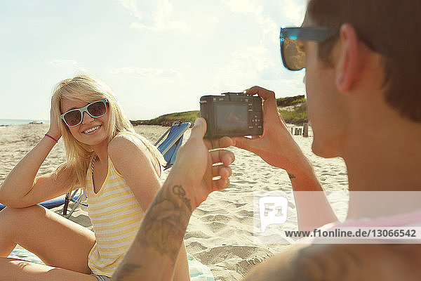 Mann fotografiert Frau  während er am Strand sitzt
