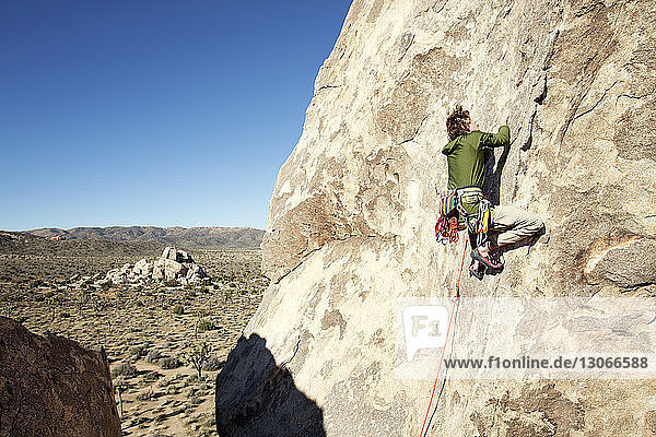 Mann klettert bei klarem Himmel an einem sonnigen Tag an einer Felsformation hoch