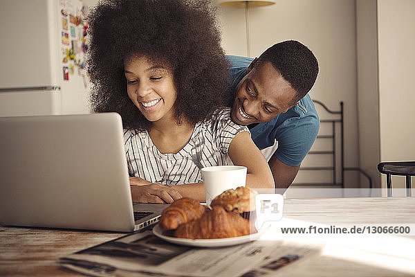 Romantic couple sitting at table with croissants and laptop computer in kitchen