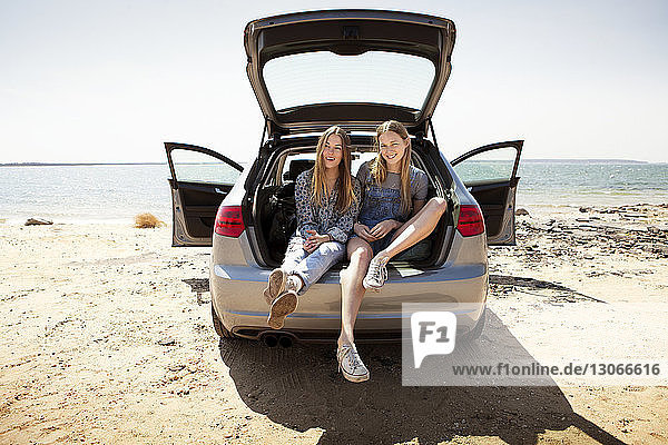 Friends sitting in car trunk against beach