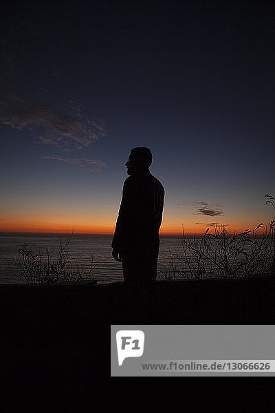 Silhouette man standing on coastal road during sunset