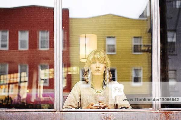 Frau schaut weg  während sie in einer Bar sitzt und durch ein Fenster gesehen wird