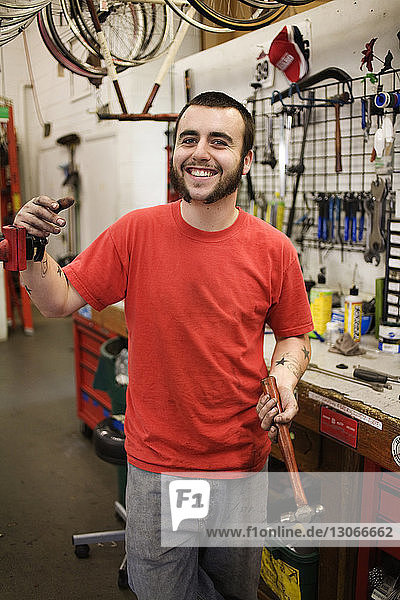Portrait of man holding hammer while standing in workshop