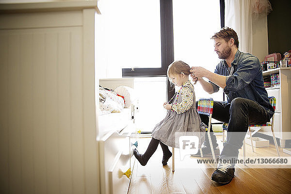 Man tying daughter's hair at home