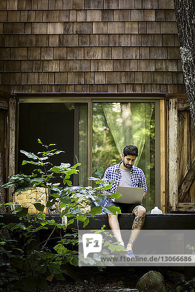 Mann benutzt Laptop-Computer  während er gegen das Haus sitzt
