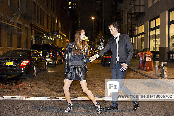 Cheerful couple holding hands and walking on city street at night