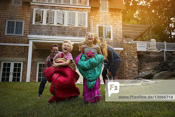 Eltern rennen hinter fröhlichen Kindern im Schlafsack gegen Haus im Hof