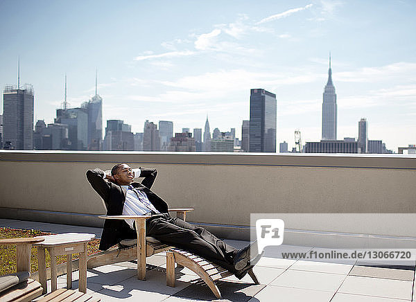 Businessman relaxing on lounge chair against sky