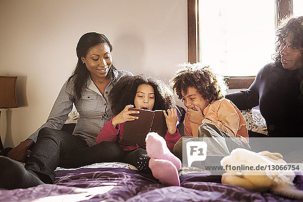 Happy family reading book while sitting on bed at home