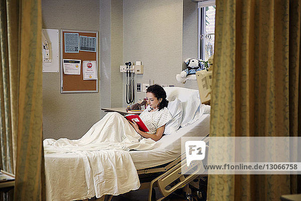 Patient reading book while sitting on bed in hospital ward