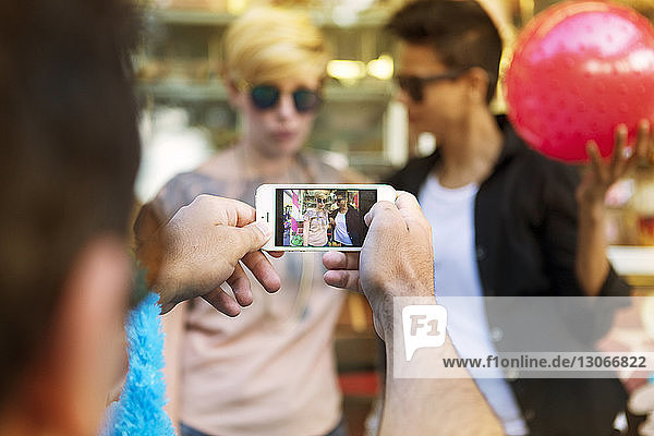 Man photographing female friends through smart phone at amusement park