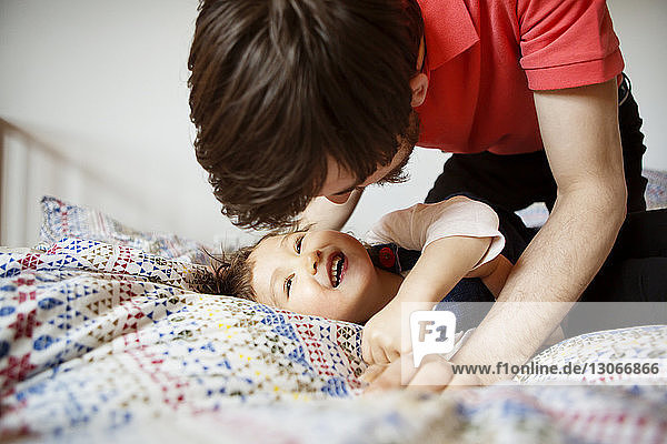 Cheerful girl playing with father while lying on bed