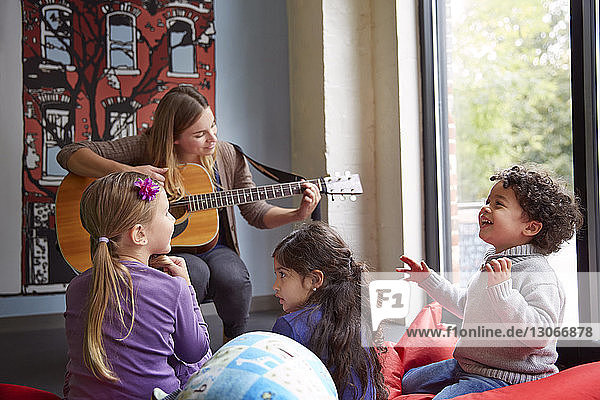 Lehrerin spielt Gitarre  während sich Kinder in der Vorschule vergnügen