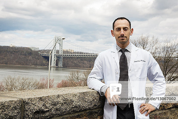 Portrait of doctor standing by retaining wall against bridge