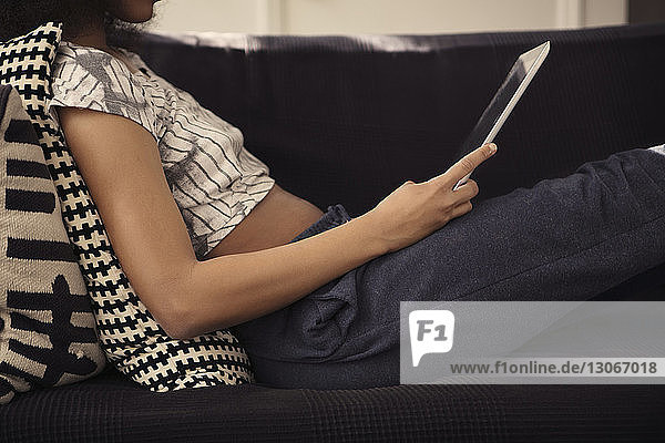 Midsection of woman using tablet computer while reclining on sofa at home