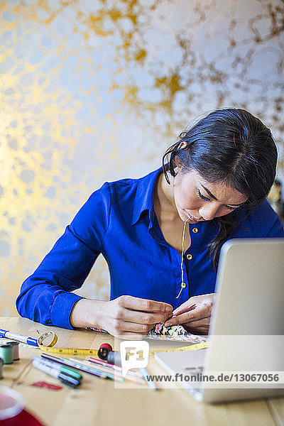Female designer stitching fabric at desk in office