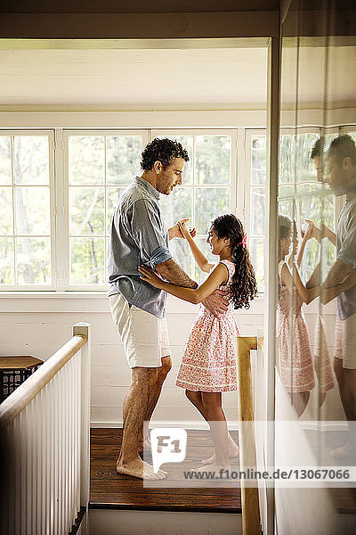 Vater und Tochter tanzen zu Hause auf dem Flur am Fenster