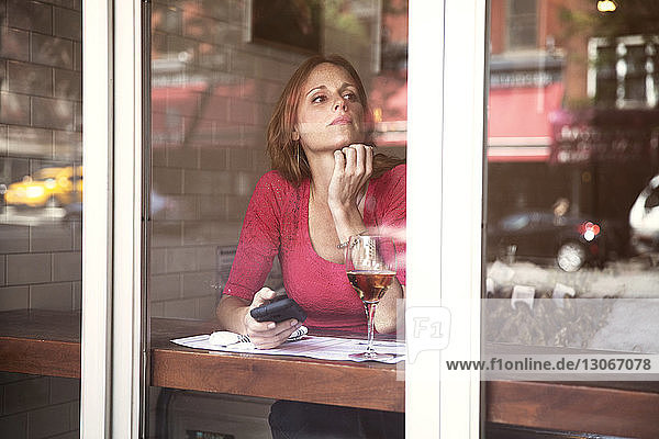 Frau schaut weg  während sie im Restaurant sitzt und durch ein Fenster gesehen wird