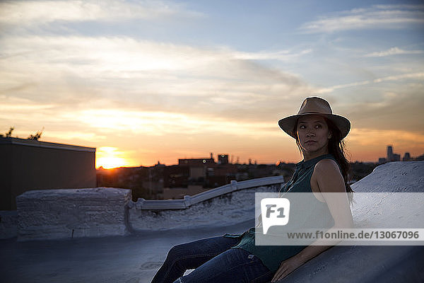 Nachdenkliche Frau lehnt bei Sonnenuntergang auf Stützmauer gegen den Himmel