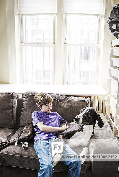 Junge mit Hund entspannt sich zu Hause auf dem Sofa