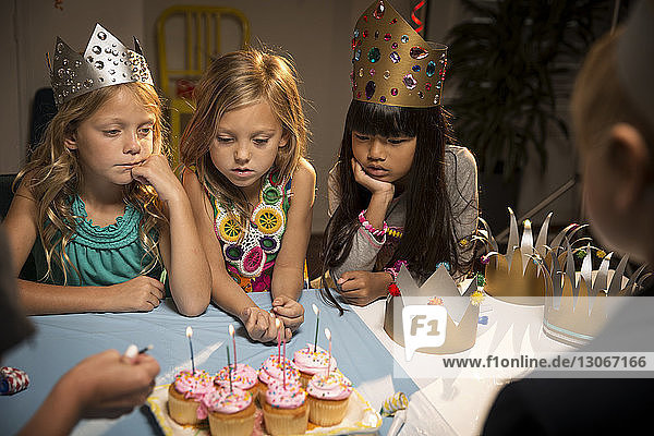 Hochwinkelansicht von Kindern  die auf Tassenkuchen auf dem Tisch schauen