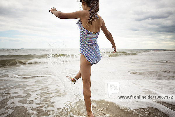 Rear view of girl playing in sea against cloudy sky