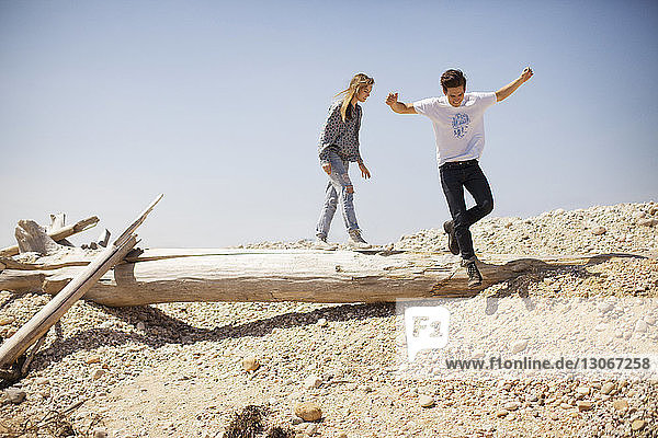 Couple jumping from log against clear sky