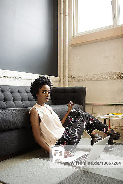 Porträt einer Frau  die einen Laptop benutzt  während sie im Büro auf dem Boden sitzt