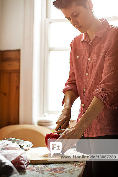 Woman cutting red bell pepper while standing by table at home