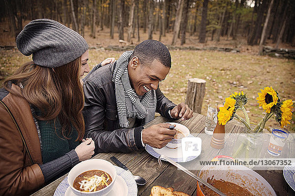 Happy couple having food while sitting at table in forest