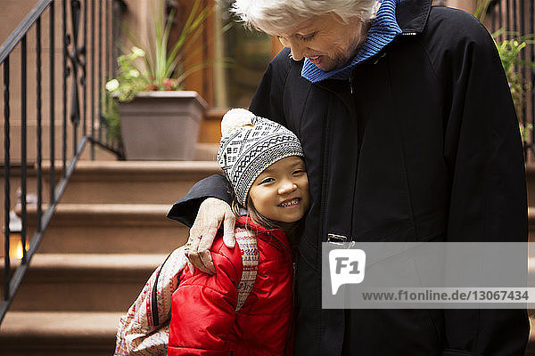 Mädchen lächelt  während es mit seiner Großmutter auf den Stufen steht